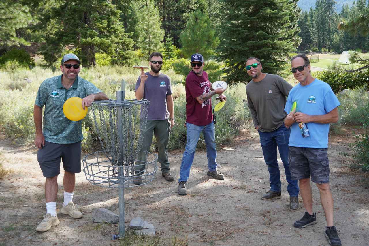 Group of disc golf players smile around the net